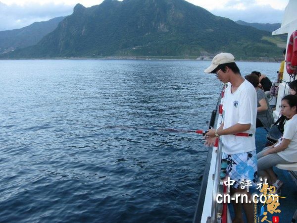 瑞芳夜钓成观光新亮点，鸿达兴6号船长小杜，为游客示范钓鱼，远方是基隆山